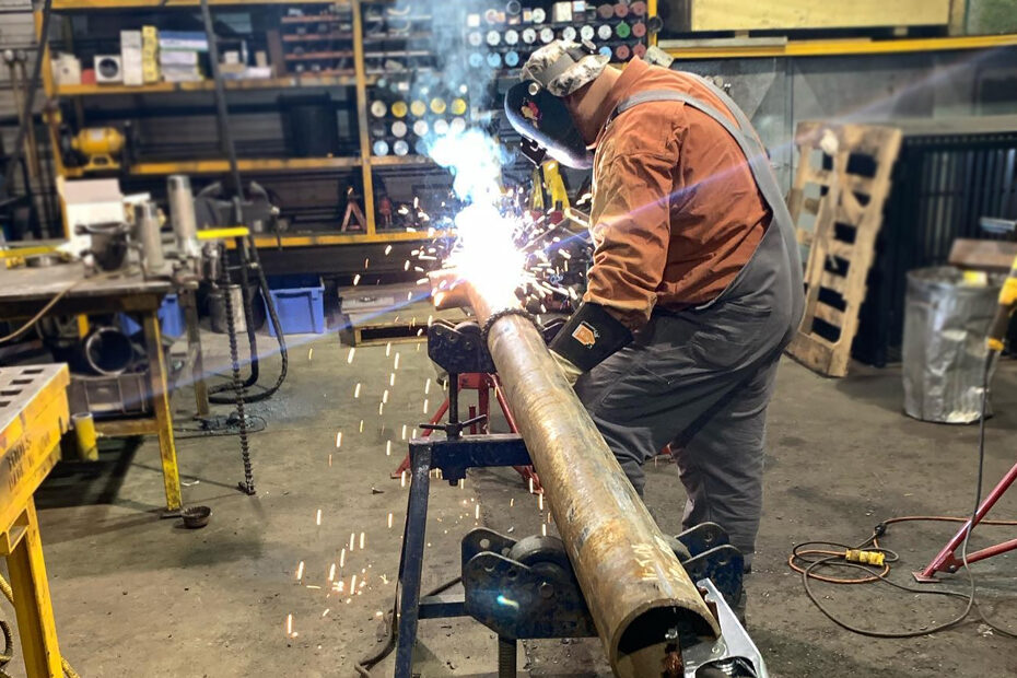 A male welder hard at work on a steel pipe