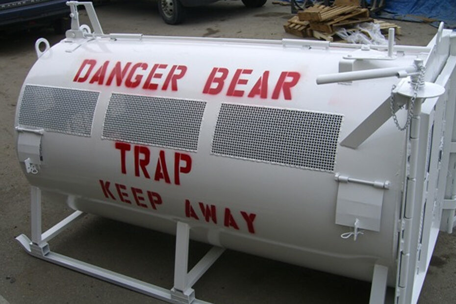 A large white bear cage or trap with a huge "danger" sign painted on it.