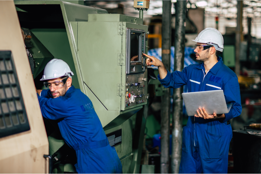 Two machinists in blue uniforms programming a CNC machine